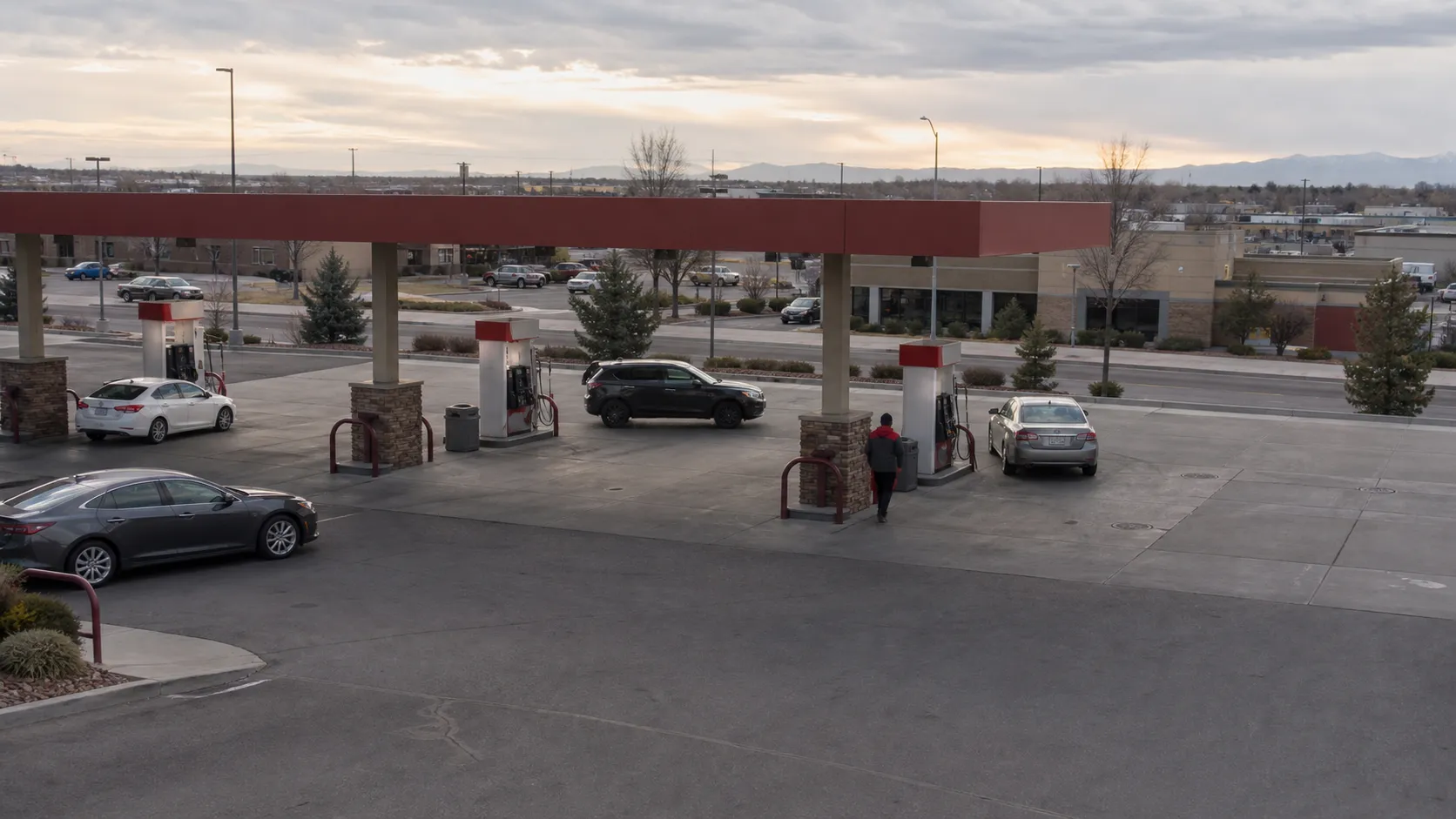 An operating fuel retail site seen from above, with several pump islands, vehicles, and the surrounding commercial area