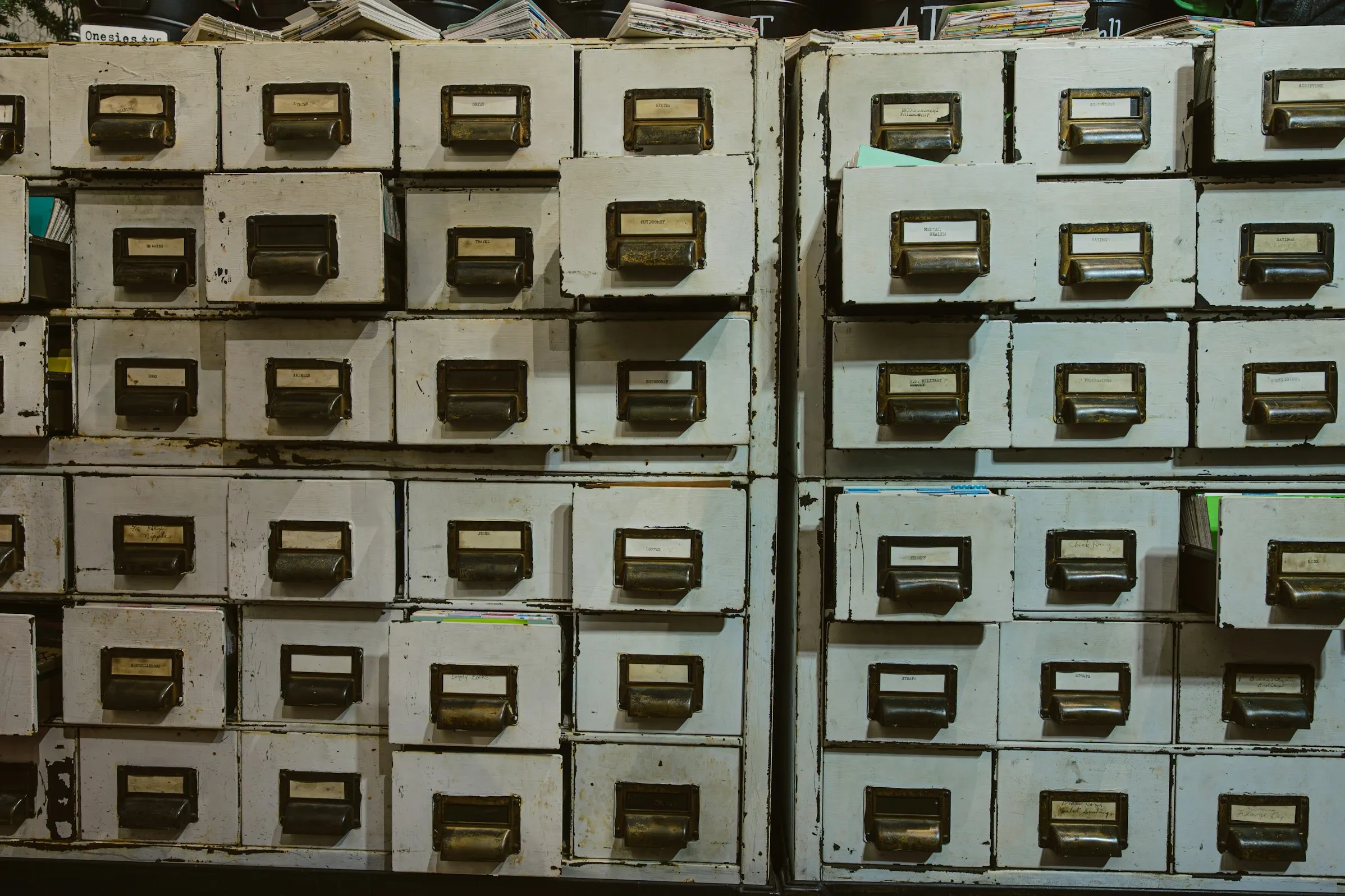 Rows of worn, cream-painted filing drawers with metal handles and small paper labels