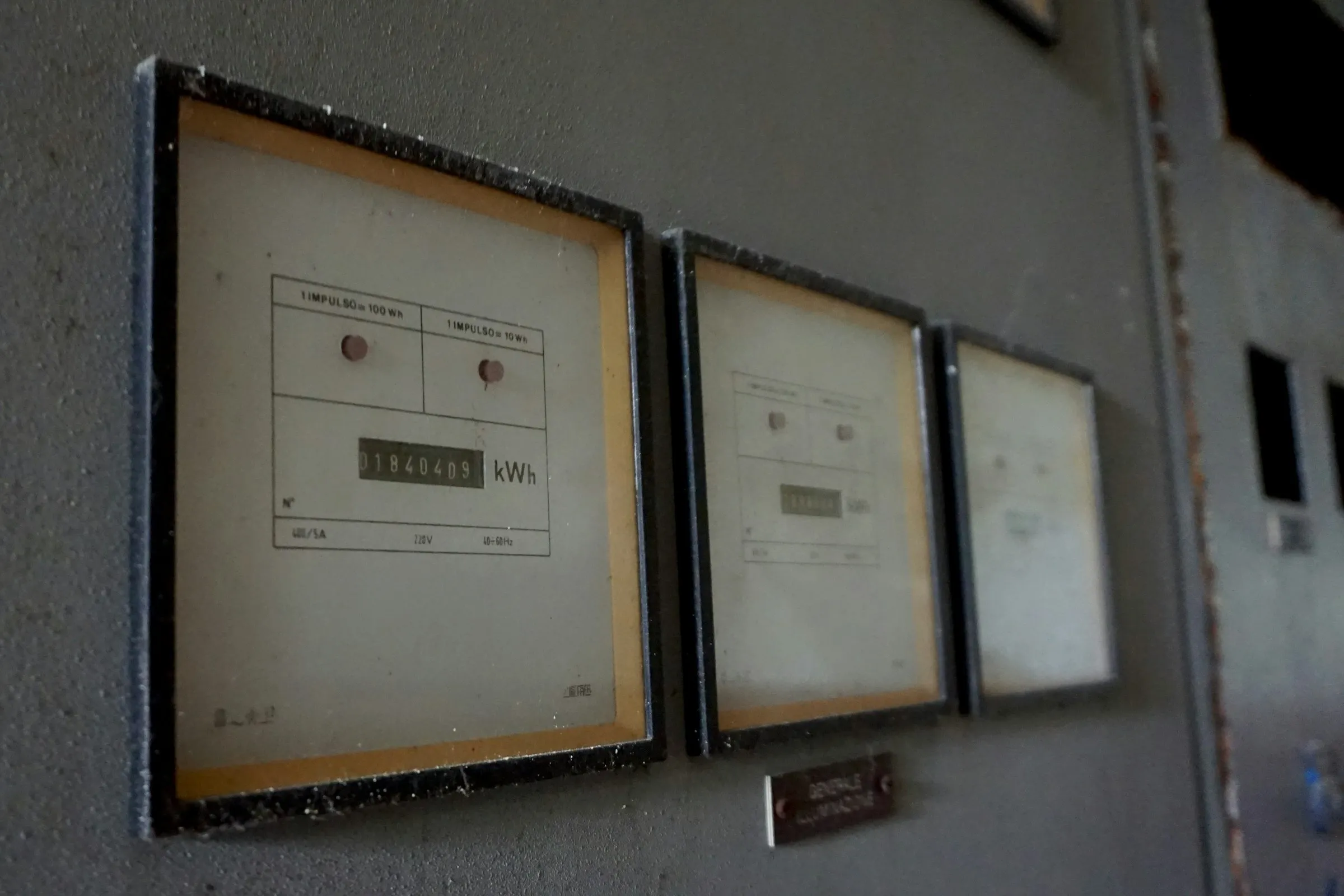 Three vintage electricity meters in black frames mounted on a gray industrial wall